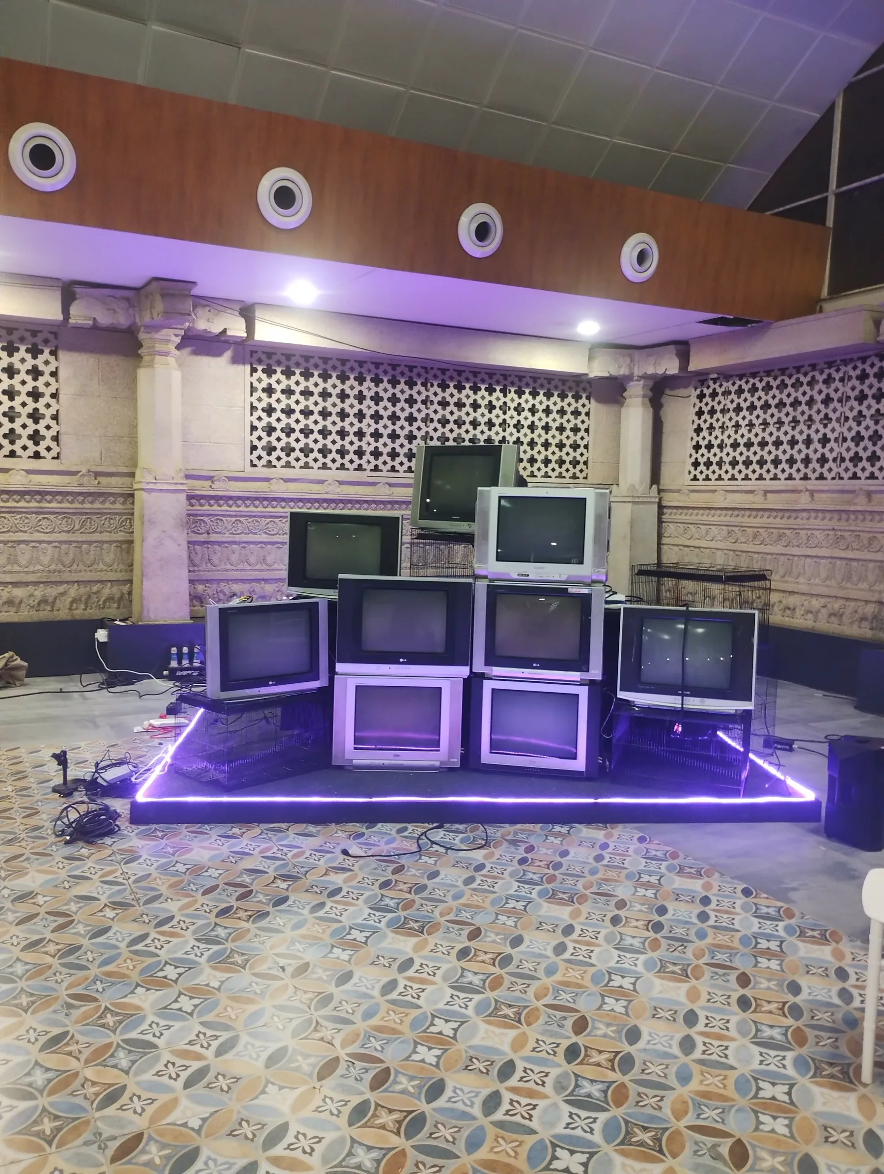 The nine-television stack lit by violet floor strips in the festival hall.